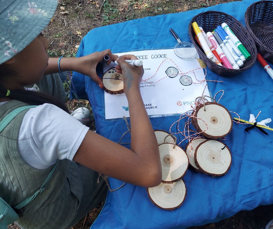 Child decorates a tree round to create a necklace.